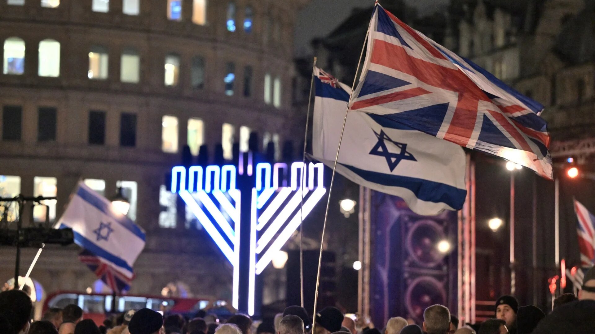 Israeli and British flags are waved as people gather for an event during the Jewish festival of Hanukkah at Trafalgar Square in central London on 16 December 2025 (AFP/Richard A Brooks)