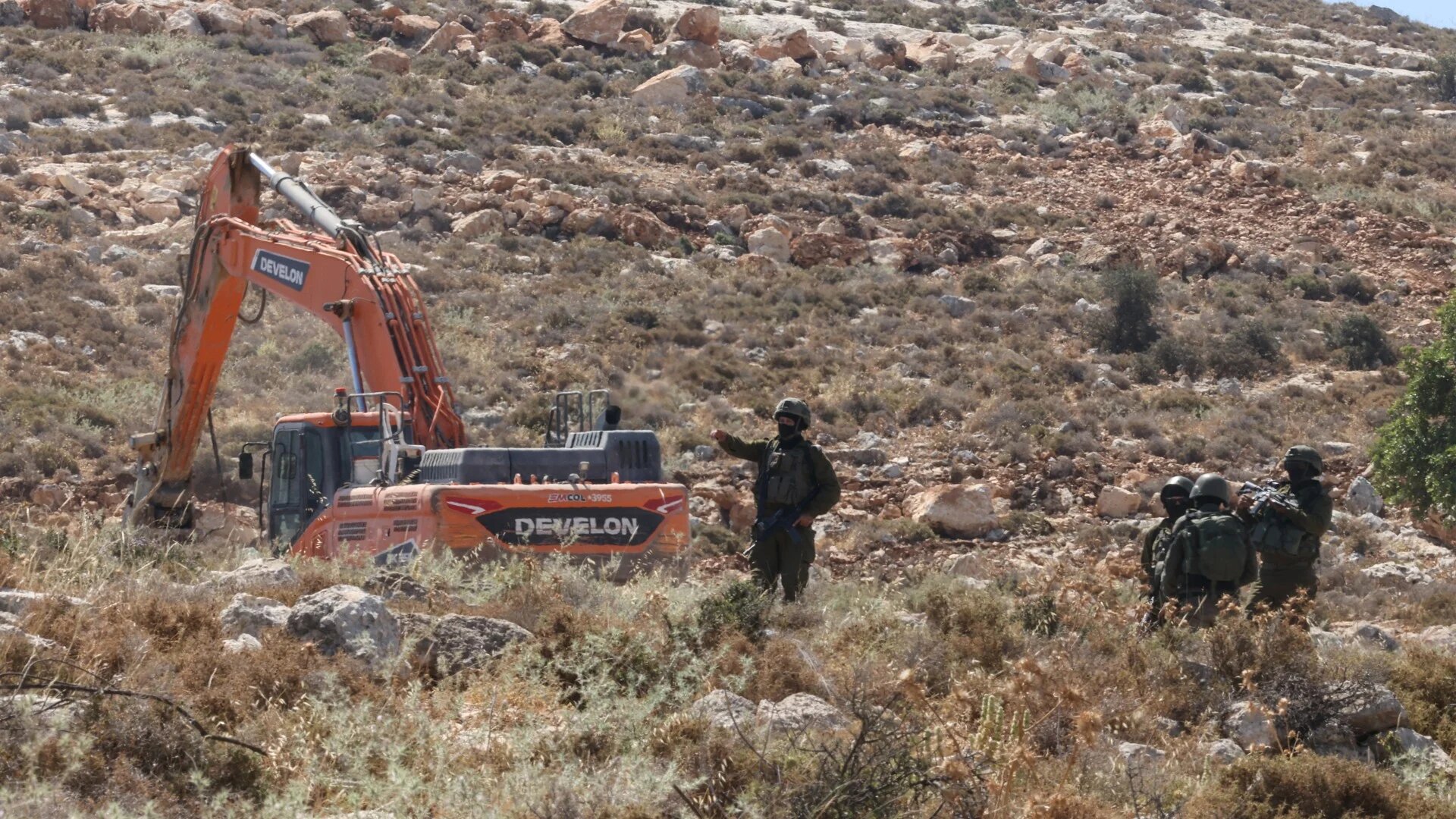 Israeli forces guard a bulldozer reportedly operating on Palestinian lands near the village of Dura, west of Hebron in the occupied West Bank, on 9 June 2026 (AFP/Hazem Bader)