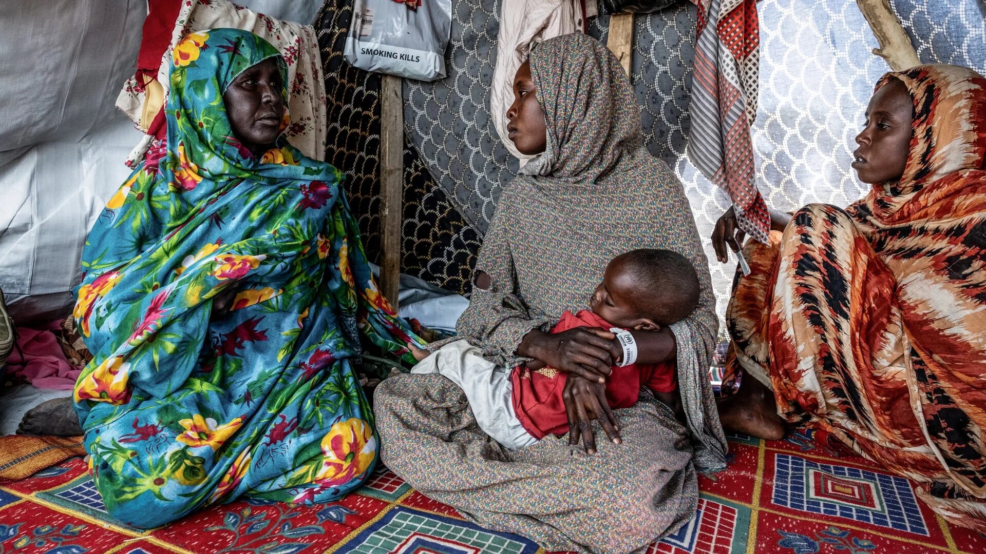 A Sudanese refugee holds her baby while sitting inside a tent at the Tine transit camp in Chad on 8 November 2025 (AFP/Joris Bolomey)