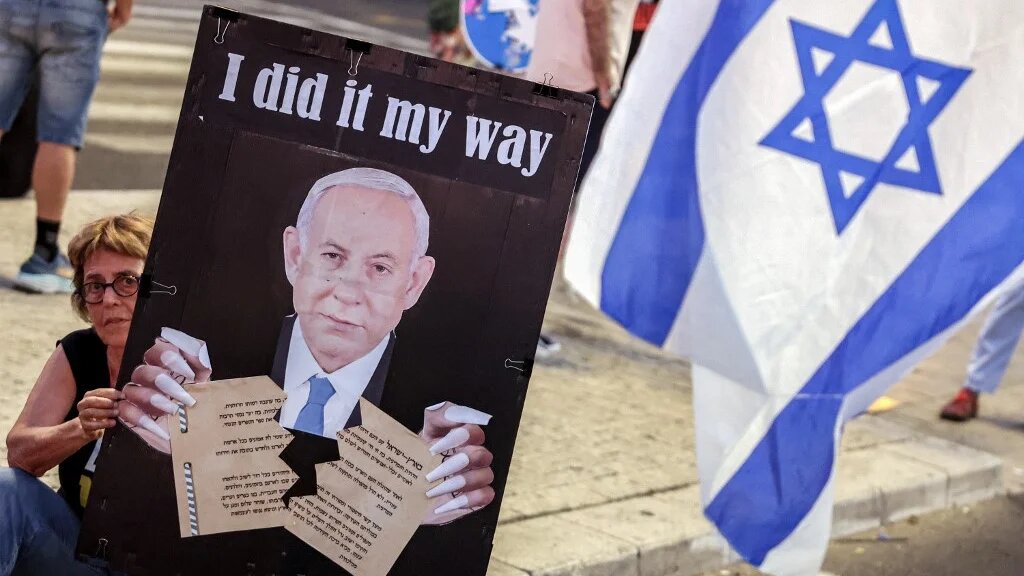 A demonstrator holds a sign depicting Benjamin Netanyahu tearing apart Israel's 1948 Declaration of Independence during a protest demanding the freeing of Israeli hostages, Tel Aviv, 24 August 2024 (Jack Guez/AFP)