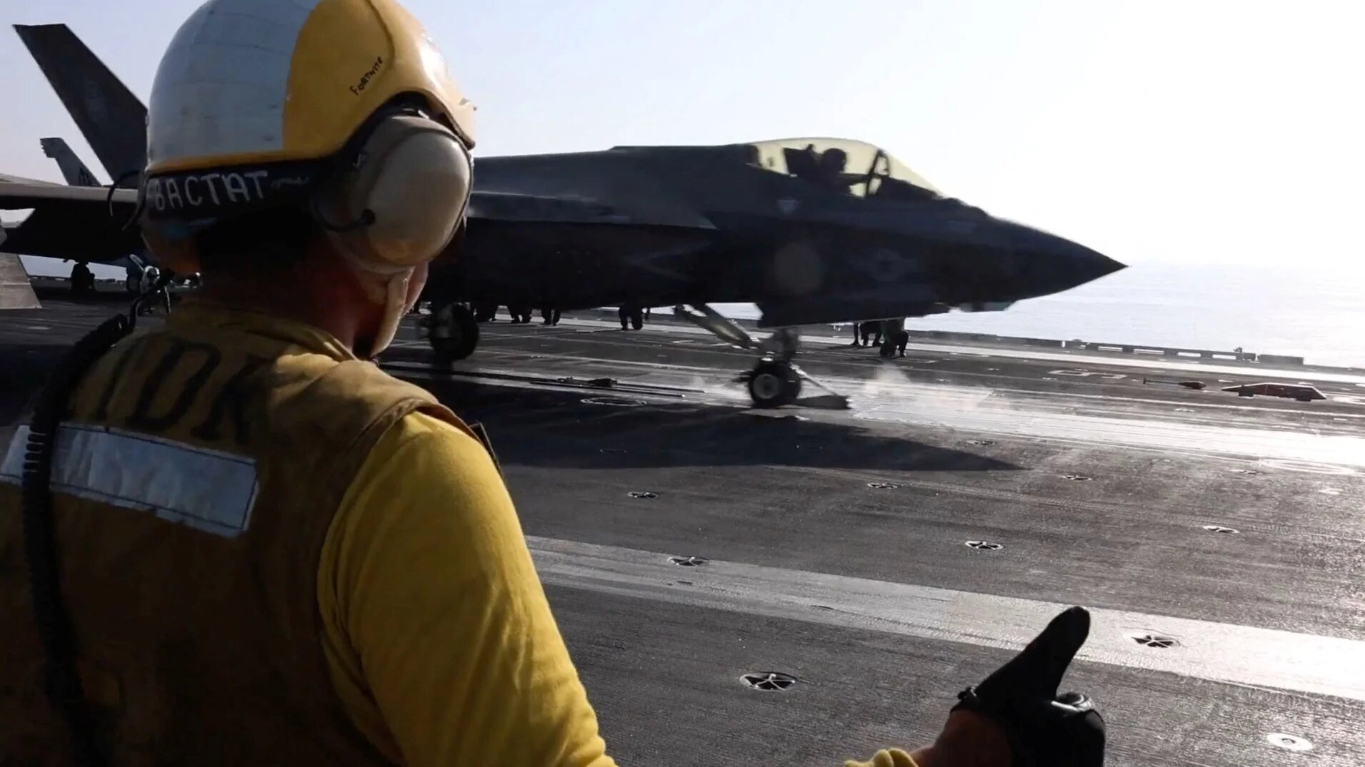 A flight deck crew member signalling an F‑35 jet on a US aircraft carrier (Centcom via Reuters)