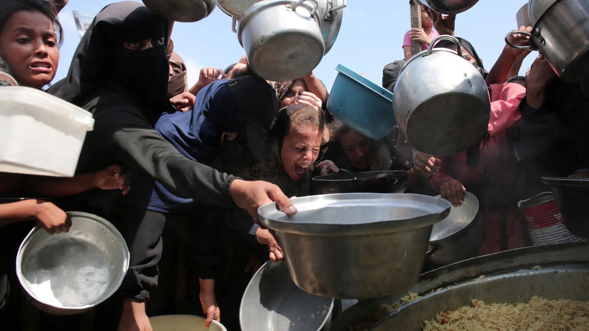 Palestinian women and children hold out their empty pots in front of a charity kitchen in Khan Younis in the southern Gaza Strip on 21 August 2025 (AFP)