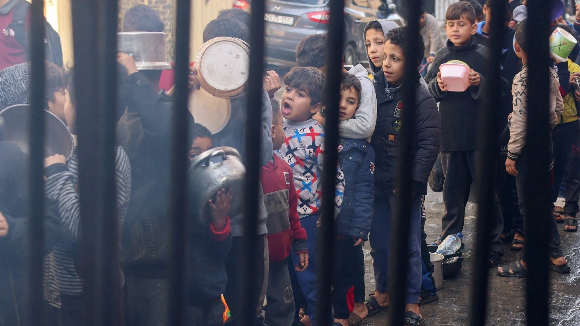 Palestinian children carry pots as they queue to receive food cooked by a charity kitchen, in Rafah, Gaza, 14 December 2023 (Reuters)