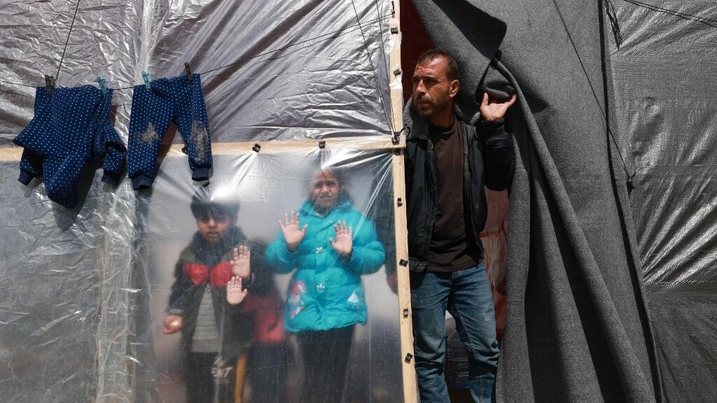 Displaced Palestinian children and a man look out from their tent in Rafah in the southern Gaza Strip on 8 March 2024 (AFP)