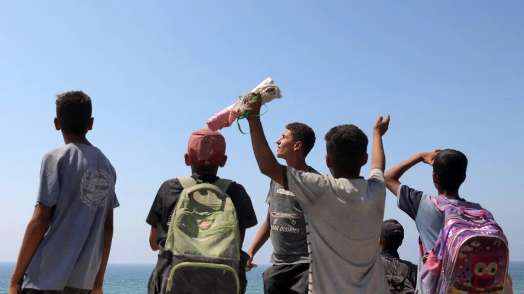 People gather as a military transport aircraft flies over the northern Gaza Strip during an aid drop on 27 July 2025 (Bashar Taleb/AFP)