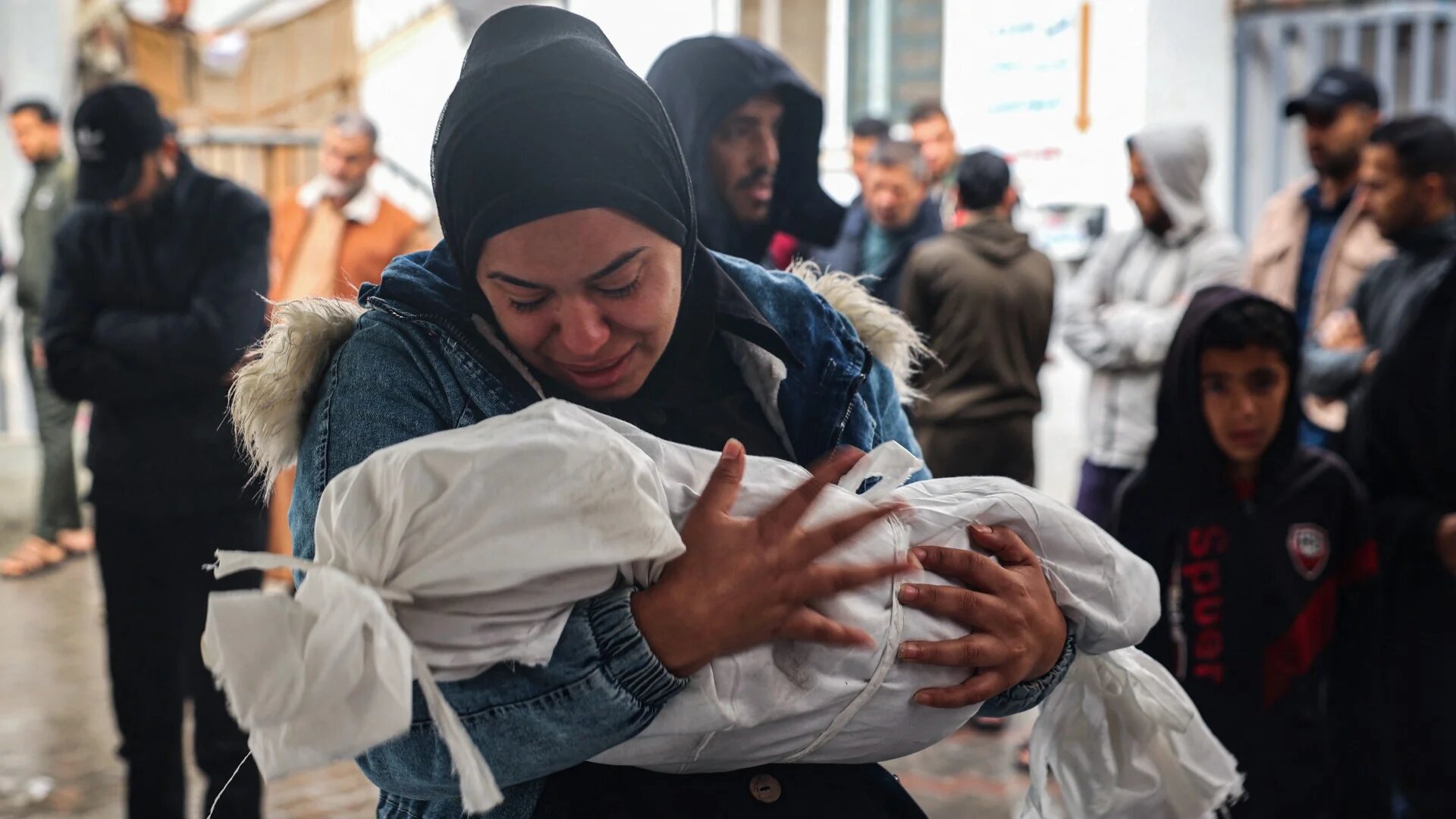 A woman mourns as she carries the shrouded body of Hani Mahmoud Qishta, killed following overnight Israeli strikes on Rafah in the southern Gaza Strip on 6 May 2024 (AFP)