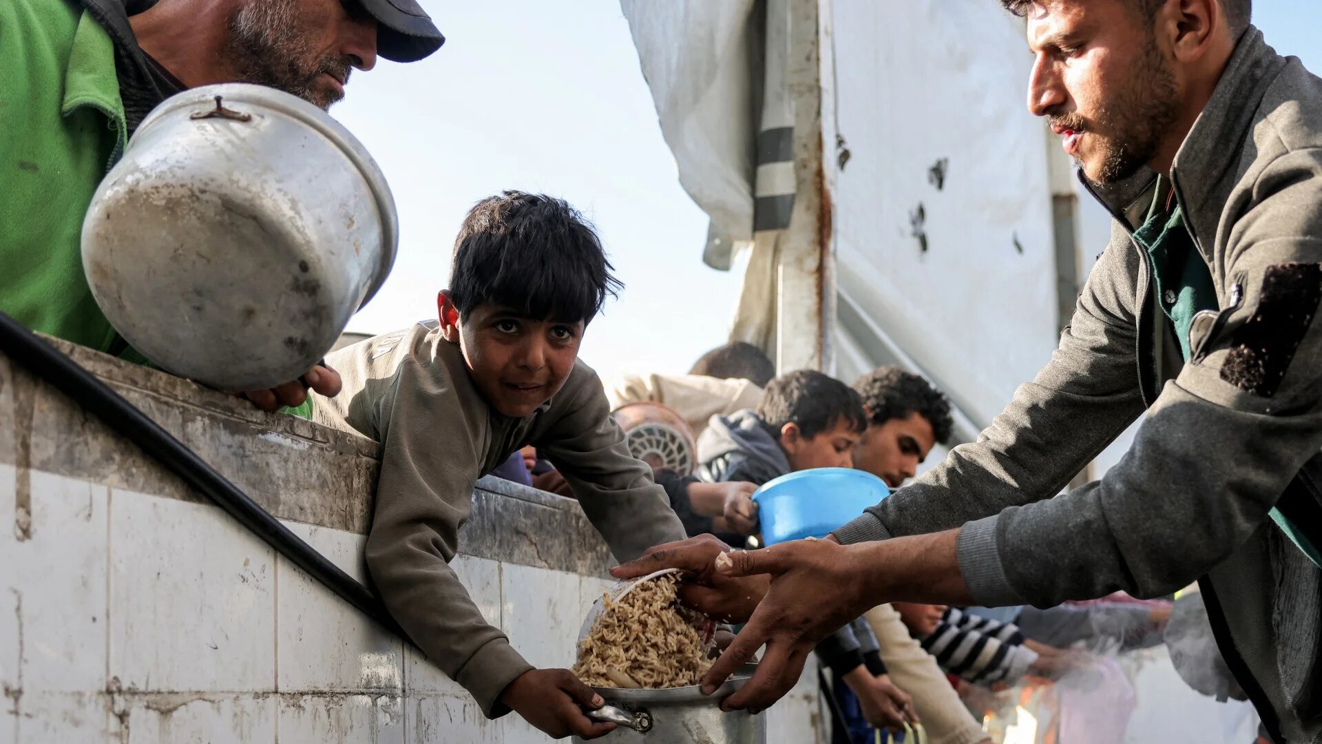 Children hold out empty pots as they queue for charity meals handed out from a kitchen during the Muslim holy fasting month of Ramadan, in Gaza City on 22 March 2025 (AFP)