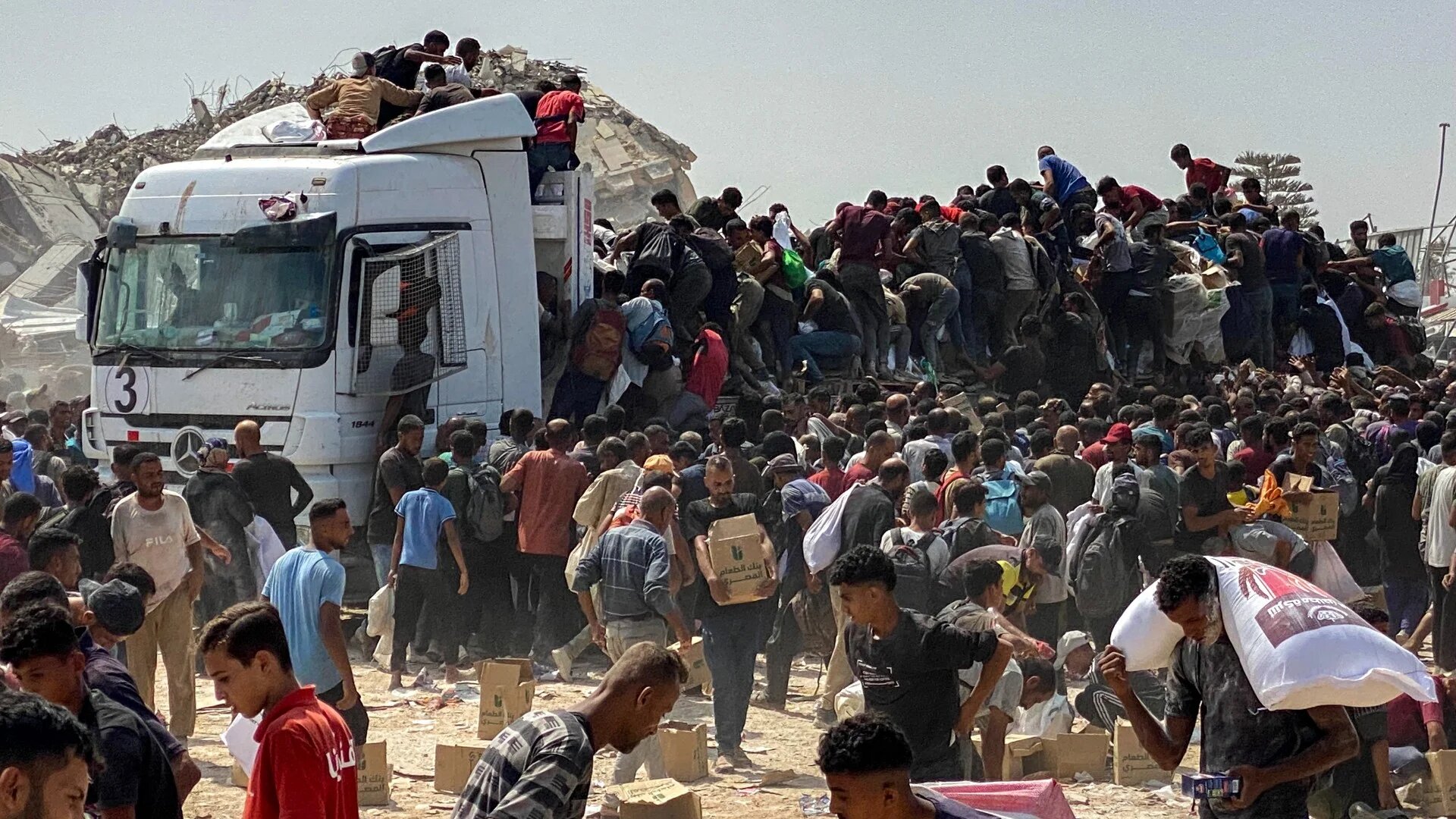 Displaced Palestinians carry food parcels as they raid trucks carrying humanitarian aid in Khan Younis, in the southern Gaza Strip on 9 August 2025 (AFP)