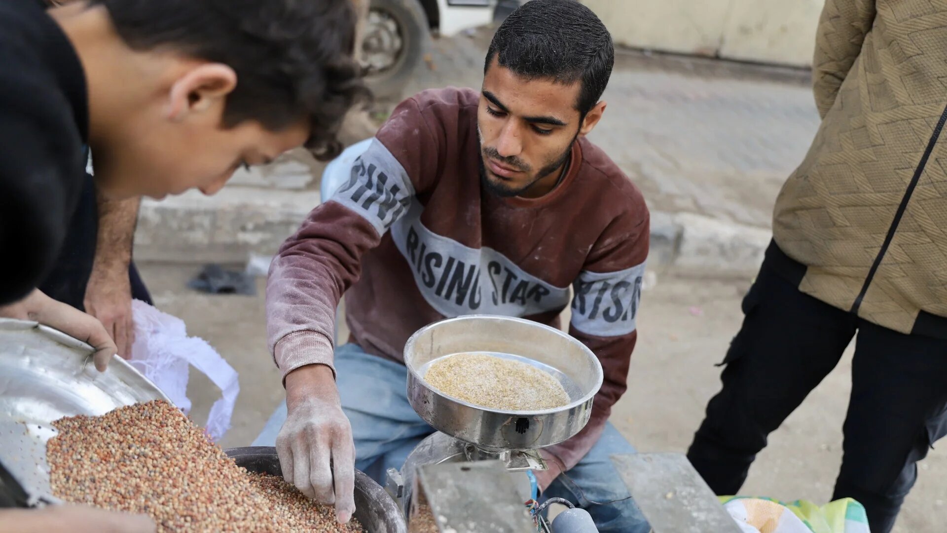 A Palestinian man sifts through grains in Gaza, amidst a heavy food shortage due to Israeli bombing and siege (Mohammed al-Hajjar)