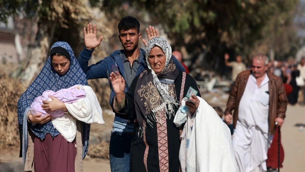Palestinians fleeing Gaza City and other parts of northern Gaza, raise their arms as they walk along a road leading to the southern areas of the enclave on 18 November 2023 (AFP)