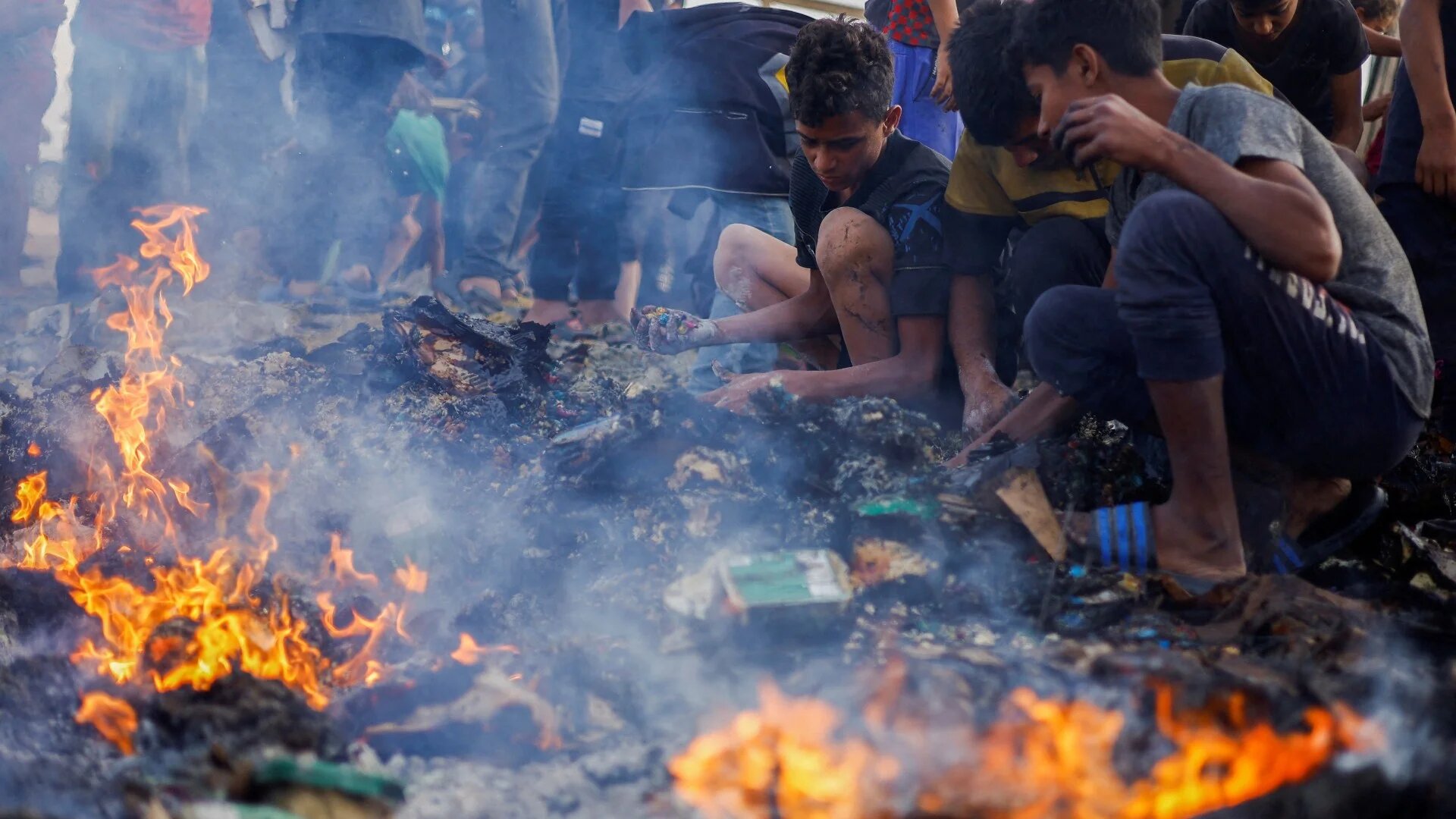 Palestinians search for food among burnt debris in the aftermath of an Israeli strike on an area designated for displaced people, in Rafah in the southern Gaza Strip, 27 May 2024 (Reuters/Mohammed Salem)