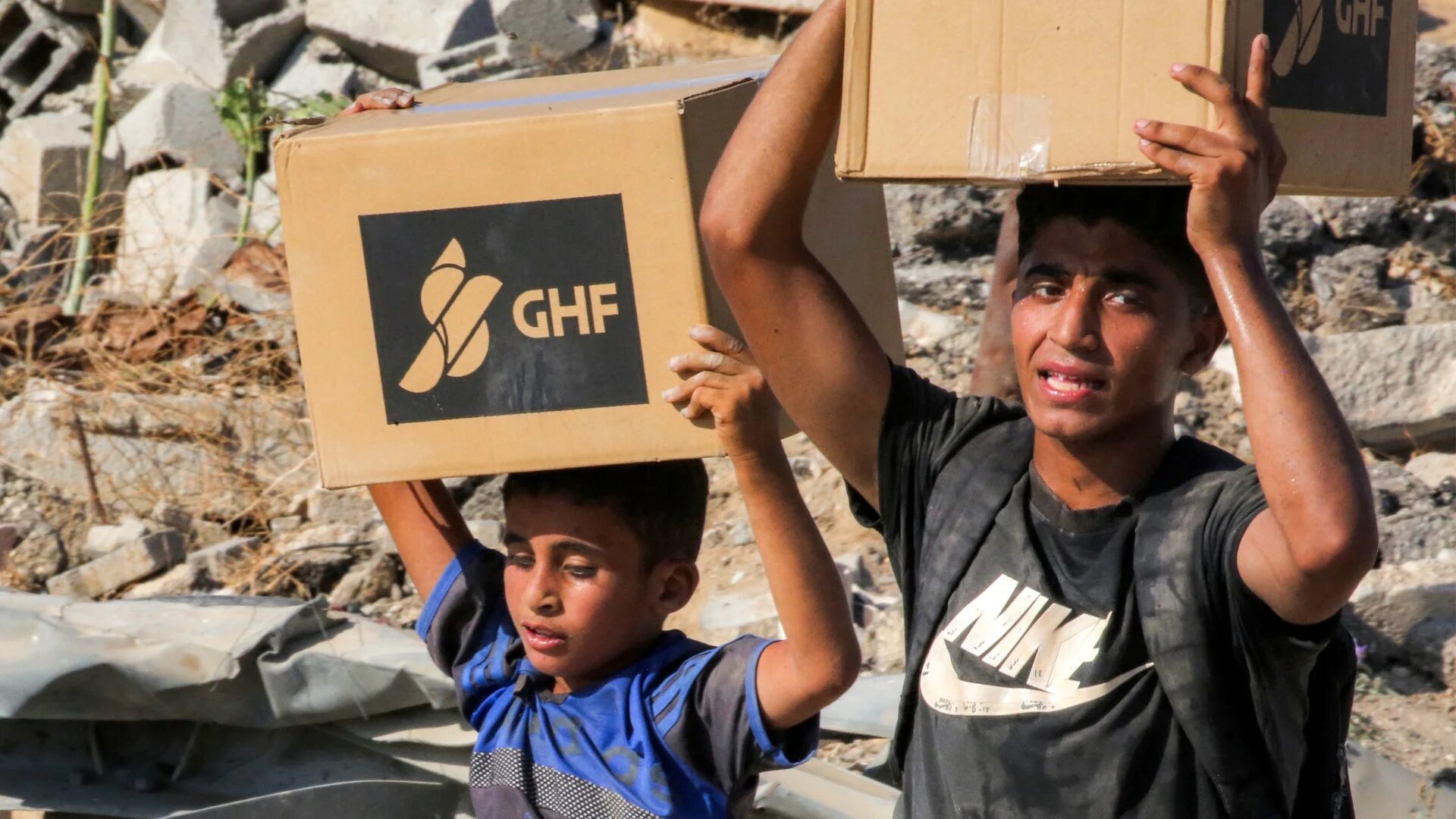 Boys walk with boxes of humanitarian aid they received at a distribution centre run by the US- and Israeli-backed Gaza Humanitarian Foundation (GHF) on 22 August 2025 (Eyad Baba/AFP)