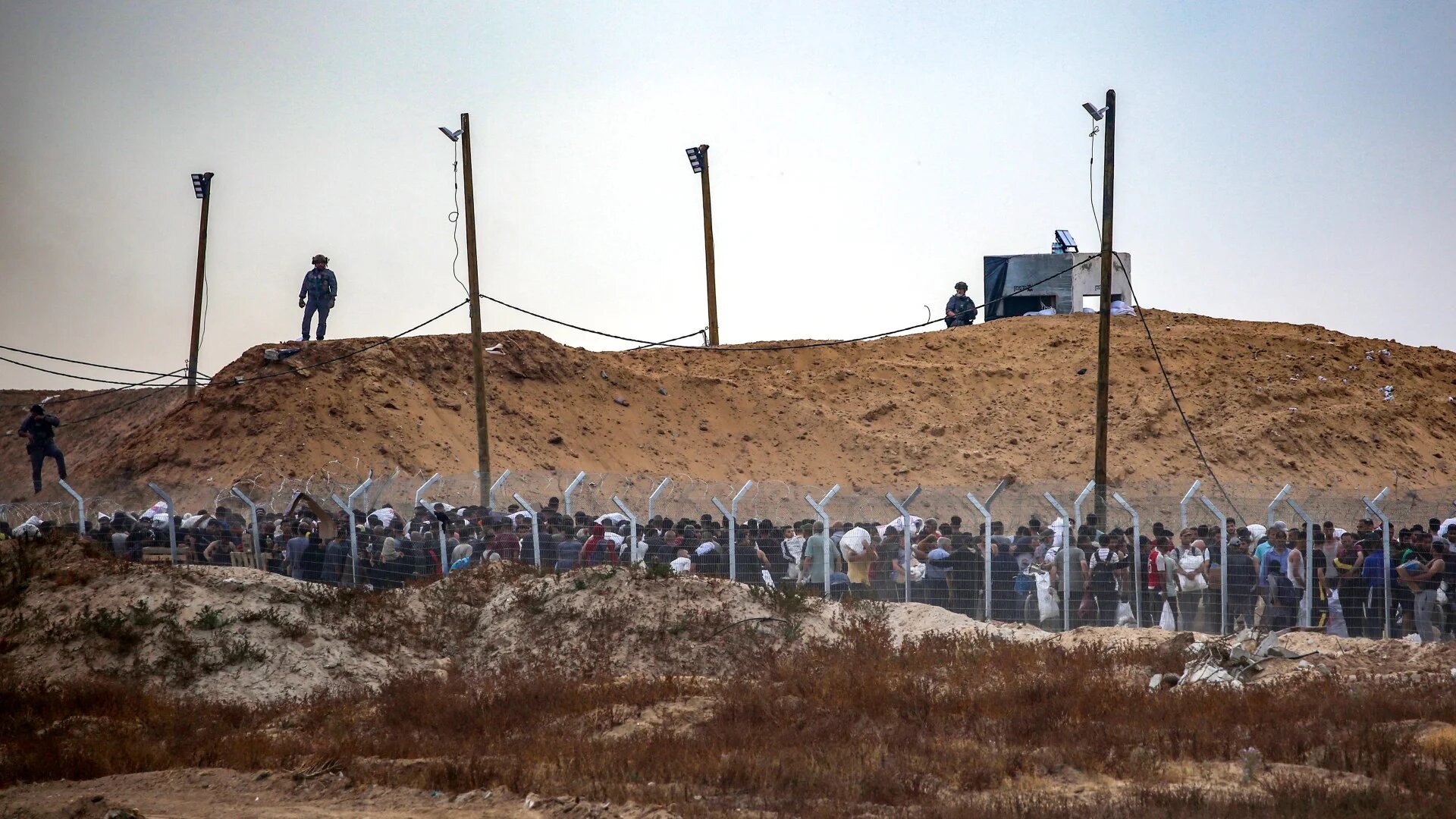 Members of a private US security company, contracted by the Gaza Humanitarian Foundation (GHF), direct displaced Palestinians as they gather to receive relief supplies at a distribution centre in the central Gaza Strip on 8 June 2025 (AFP/Eyad Baba)