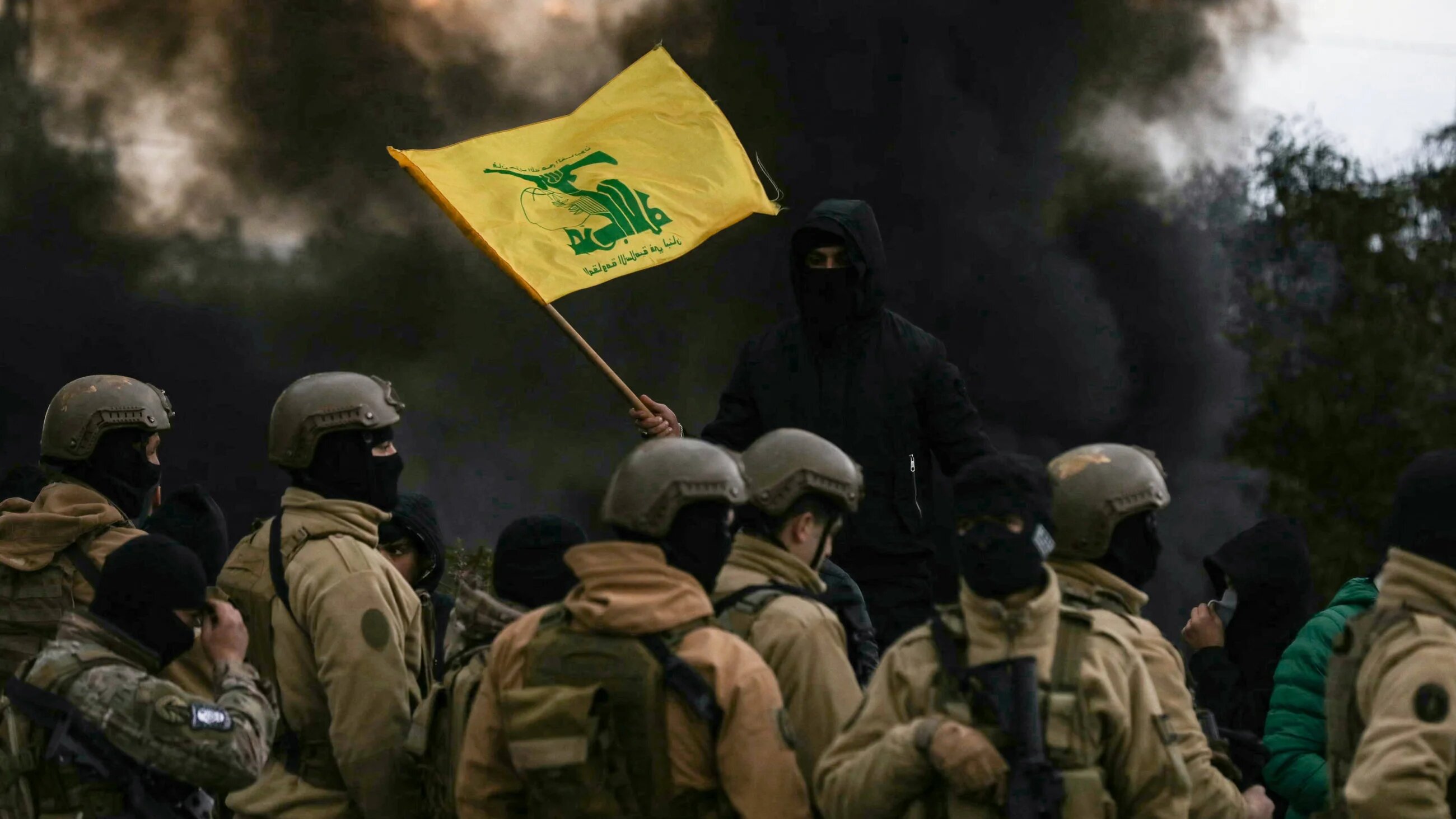 A Hezbollah supporter waves the group's flag in front of Lebanese army troops, as protesters burn tyres to block the road leading to Beirut’s international airport, on 7 February 2025 (AFP)