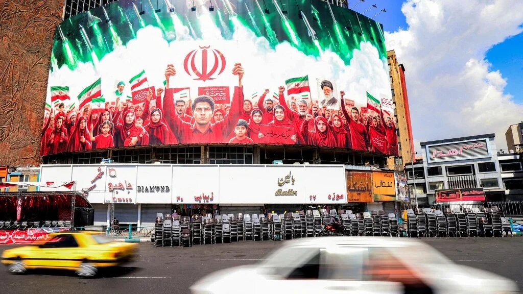 A banner depicts missiles being fired behind Iranians who are rallying in solidarity with the government, at Valiasr Square in Tehran on 6 April 2026 (Atta Kenare/AFP)