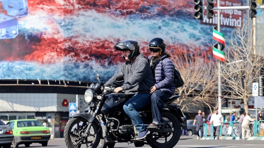 Iranians ride past an anti-US billboard in Tehran on 17 February 2026 (Atta Kenare/AFP)