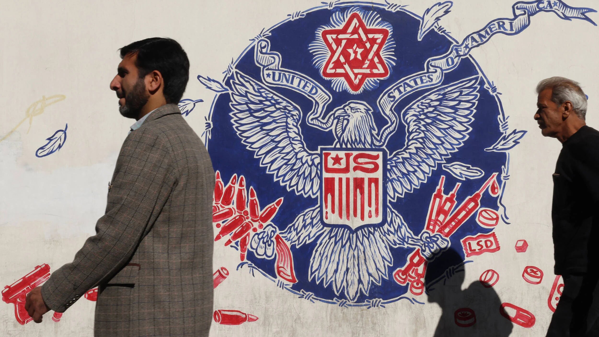 Iranians walk past a mural depicting a mock version of the Great Seal of the United States painted on the outer walls of the former US embassy in Tehran on 6 November 2024 (AFP)