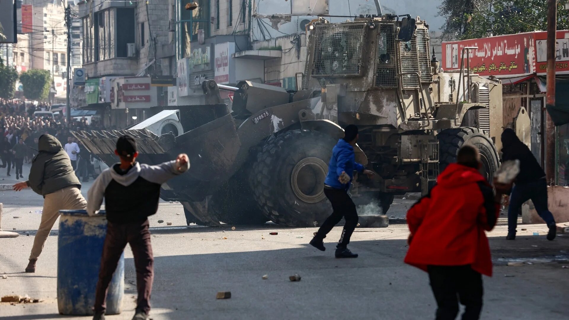Palestinians hurl rocks at an army bulldozer, during a deadly Israel raid in the occupied West Bank city of Jenin on 26 January 2023 (AFP)