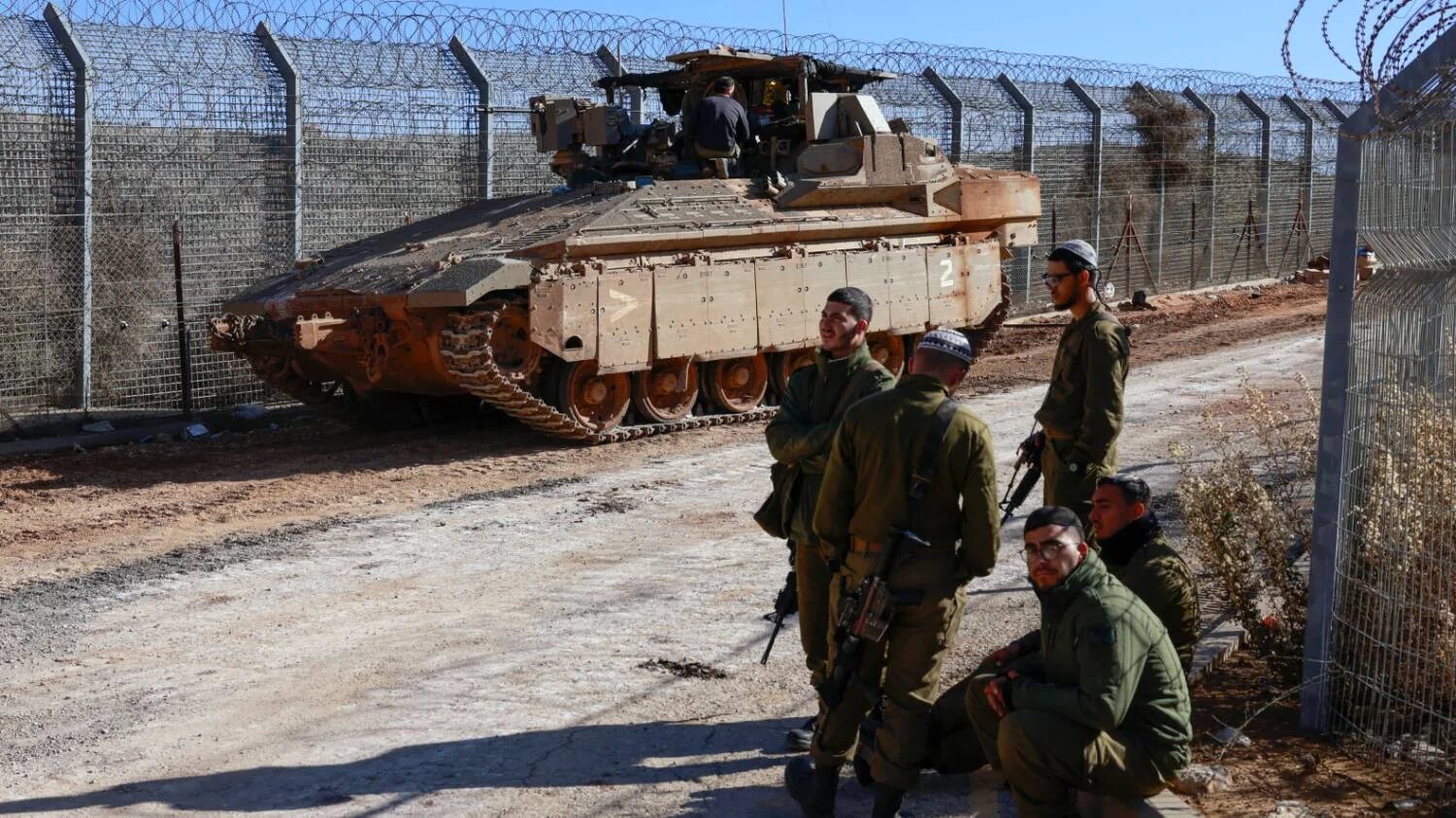 Israeli soldiers stand on the fence with the buffer zone that separates the Israeli-occupied Golan Heights from Syria, on 9 December 2024.