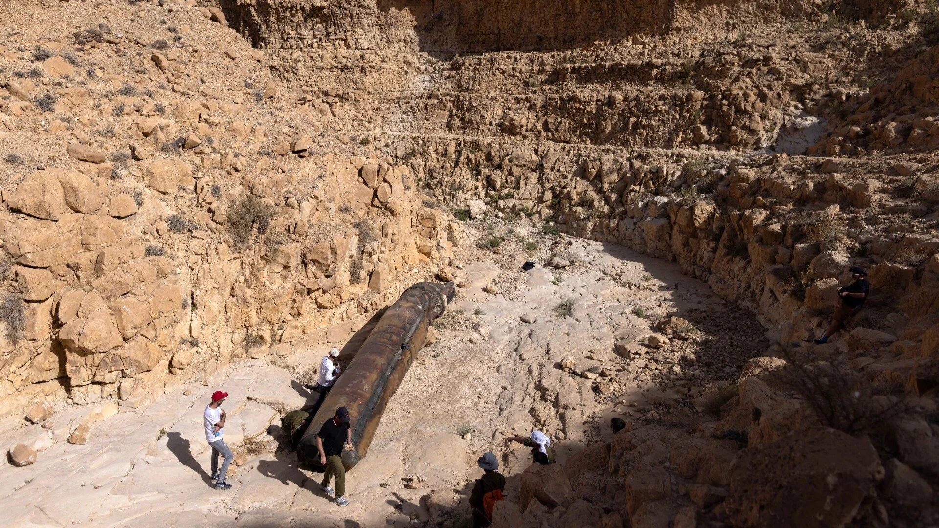 Israeli plain-clothed military personnel examine a part of an Iranian ballistic missile, recently located in an open area near the city of Arad in southern Israek, on 24 April 2024 (AFP/Oren Ziv)