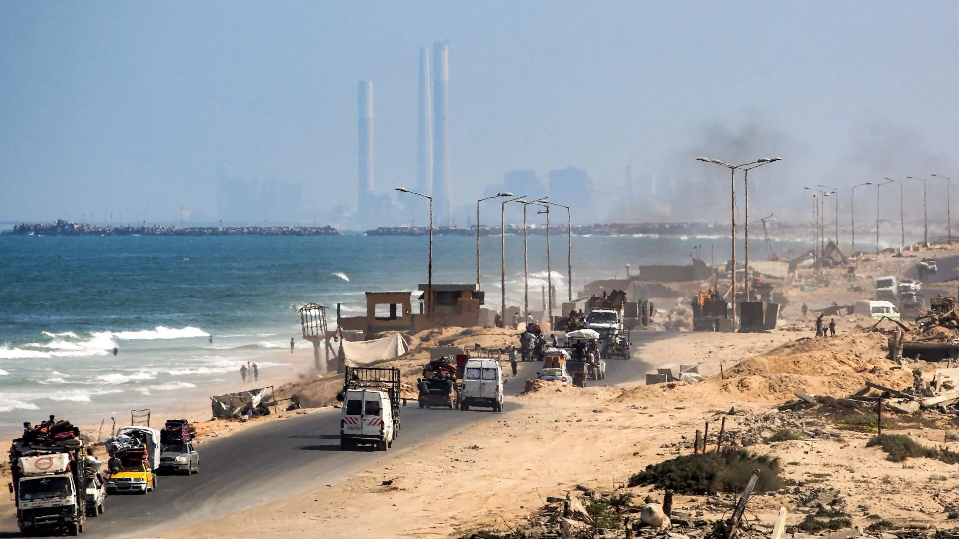 Israel's Rutenberg power station in Ashkelon is pictured in the background as vehicles move along the coastal road in Nuseirat in the central Gaza Strip, on 9 September 2025 (AFP/Eyad Baba)