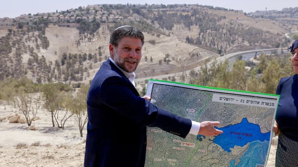 Israeli Finance Minister Bezalel Smotrich displays a map of the E1 corridor, outside Jerusalem in the occupied West Bank, on 14 August 2025 (Menahem Kahana/AFP)