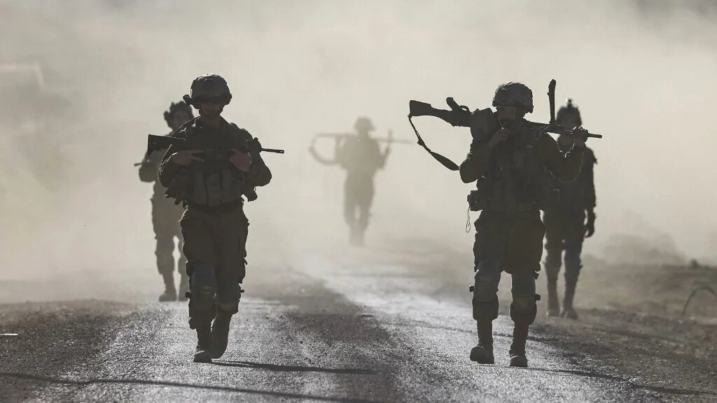 Israeli soldiers walk near the entrance to the Gaza Strip on 12 March 2024 (Menahem Kahana/AFP)
