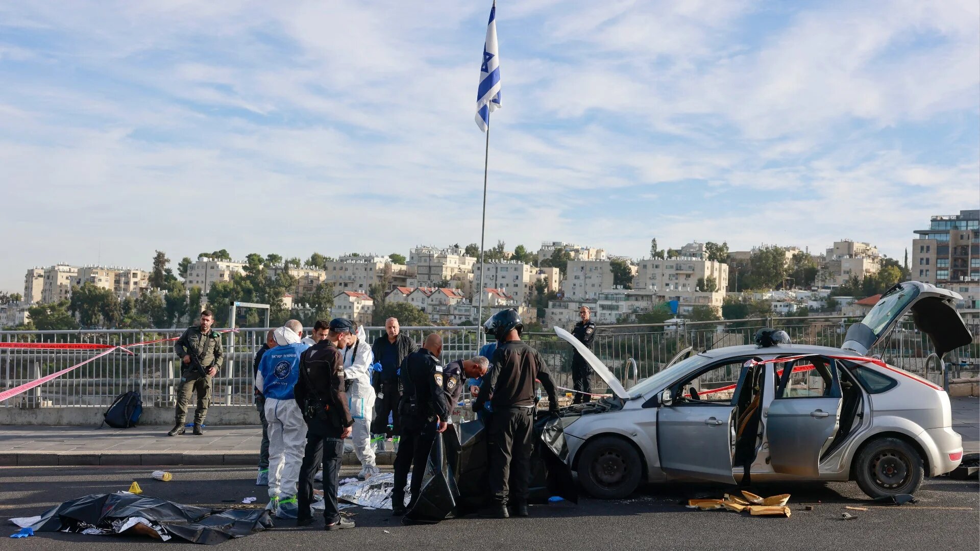 Israeli police and security forces stand next to the covered bodies of suspected attackers as they secure the site of a shooting in Jerusalem on 30 November 2023 (AFP)