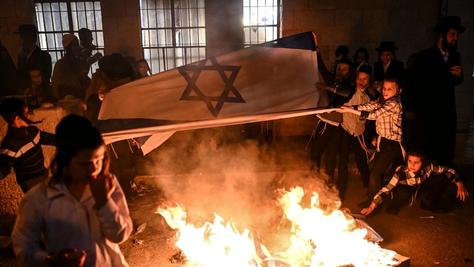  Members of the anti-Zionist Hassidic group Neturei Karta burn Israeli flags during a rally in Jerusalem on 14 May 2024 (AFP)