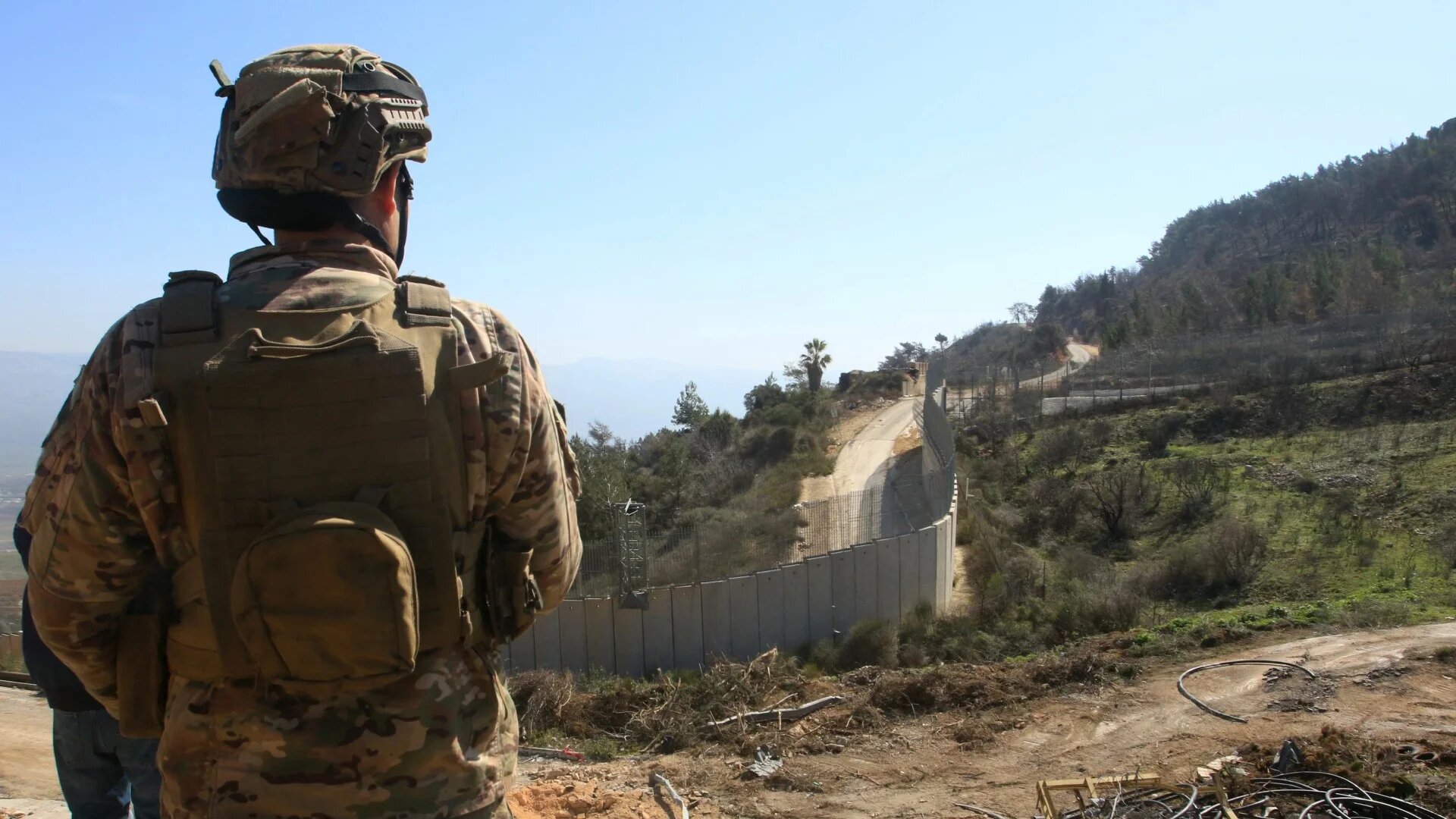 A Lebanese soldier overlooks the border wall with Israel with a newly installed Israeli army outpost in the distance in an area where the Israeli army did not withdraw on 18 February (Mahmoud Zayat/AFP)