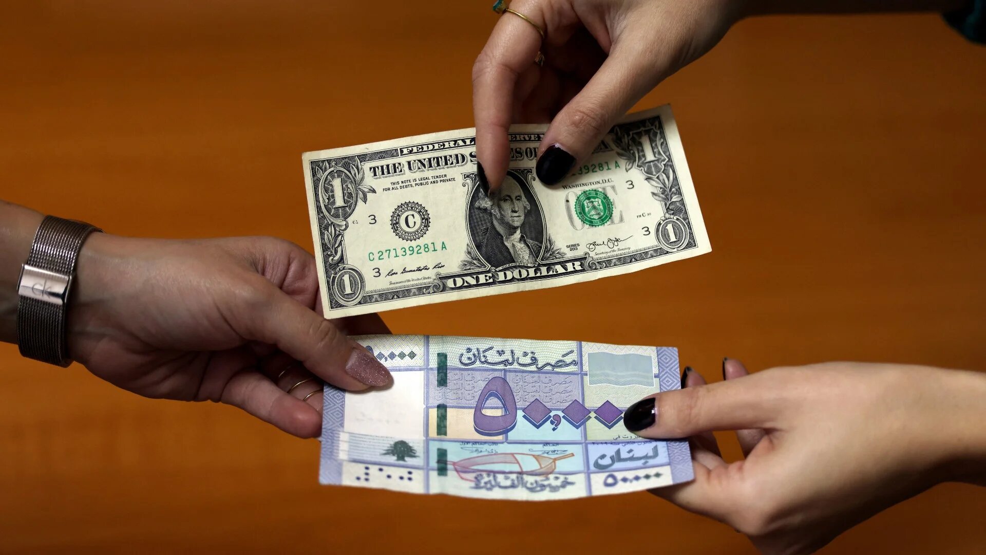 In this file photo taken on 19 January 2023, two women exchange a one US dollar bill against a 50 thousand Lebanese lira banknote, in Beirut (AFP)
