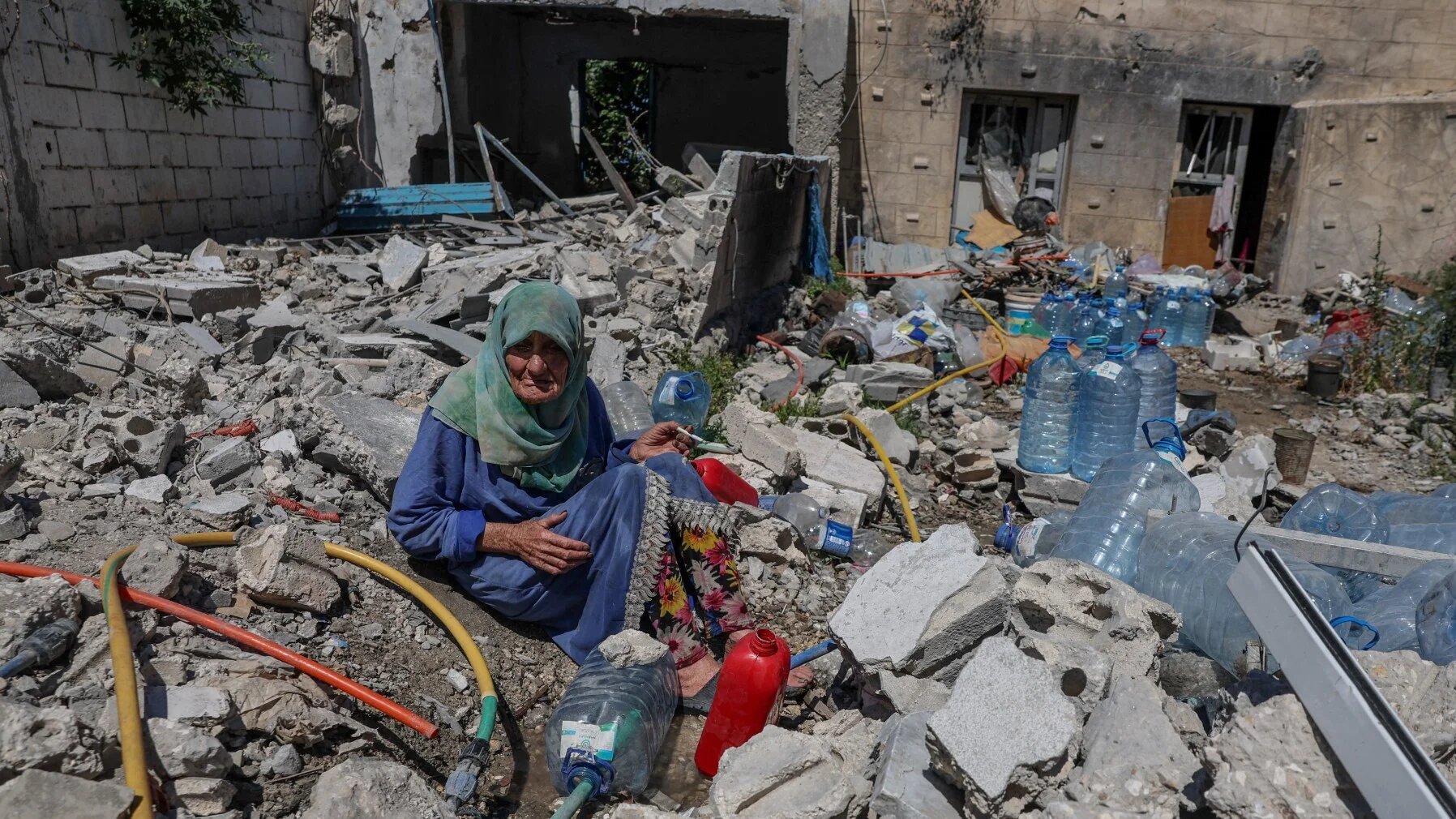 Khadija Amara, whom local residents said had not left her home, fills a jerrycan with water as she sits among the rubble of a house, which was damaged by an Israeli strike, in Qlaileh in the Tyre district, southern Lebanon, June 19, 2026. REUTERS/Zohra Bensemra TPX IMAGES OF THE DAY
