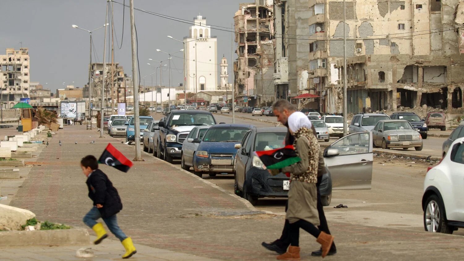 Libyans hold up national flags as they walk past damaged buildings on 17 February 2022 in Libya's eastern city of Benghazi.