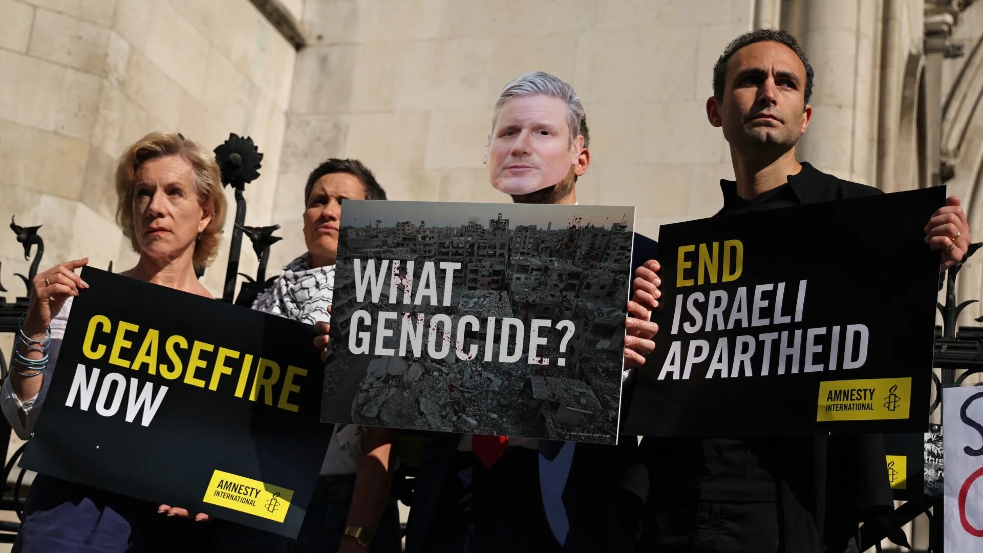 A person dressed as Britain's Prime Minister Keir Starmer (C) holds a placard beside British actors and activists, Khalid Abdalla (R) and Juliet Stevenson (L) outside the Royal Courts of Justice alongside other Pro-Palestinian activists and supporters in central London on 13 May 2025 (AFP)