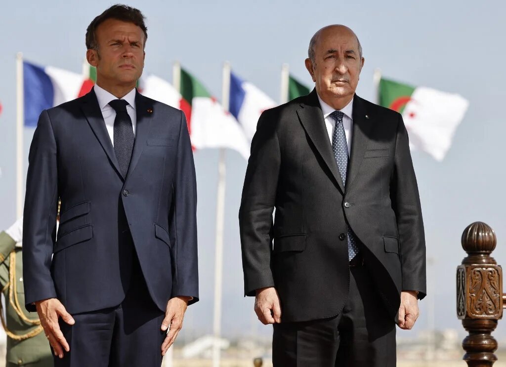 Emmanuel Macron et Abdelmadjid Tebboune écoutent les hymnes nationaux de leurs pays, à l’aéroport d’Alger le 27 août 2022 (AFP/Ludovic Marin)