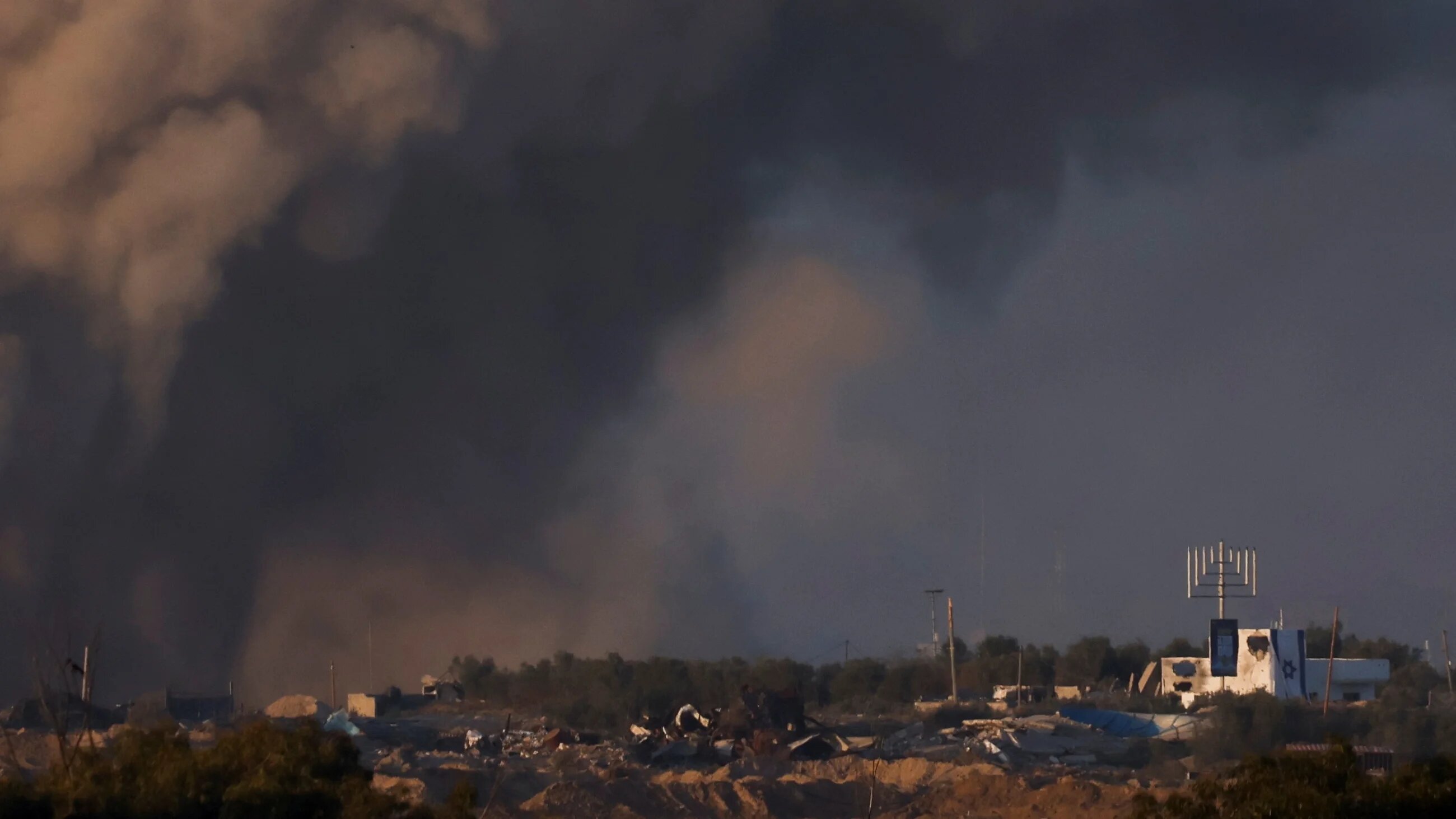 A Hanukkah menorah stands next to an Israeli flag inside central Gaza following an airstrike, as seen from southern Israel, on 11 December 2023 (Amir Cohen/Reuters)
