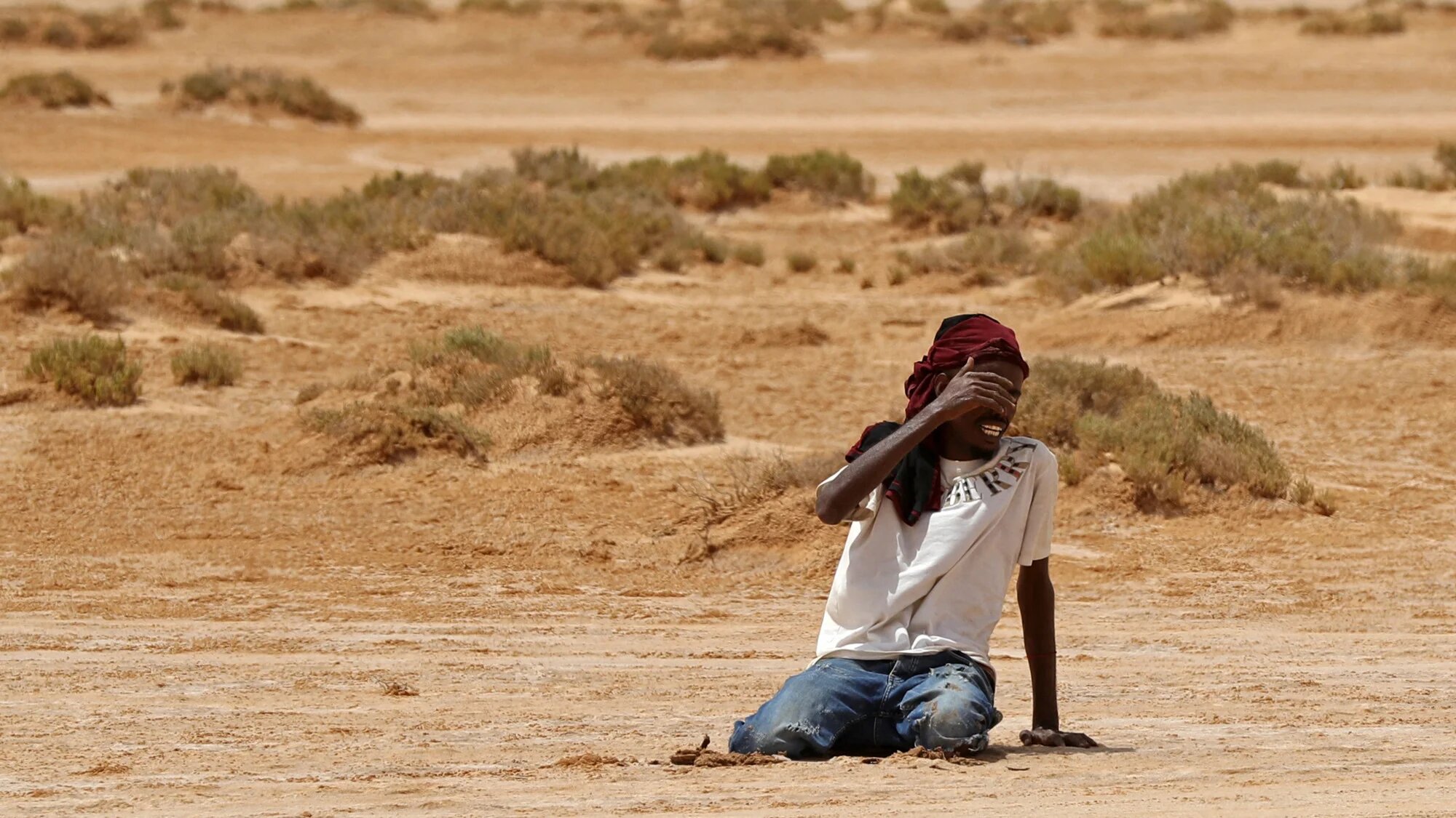 A Sub-Saharan man collapses due to exhaustion and dehydration upon his arrival in an uninhabited area near al-Assah on the Libya-Tunisia border on July 30, 2023 (AFP)