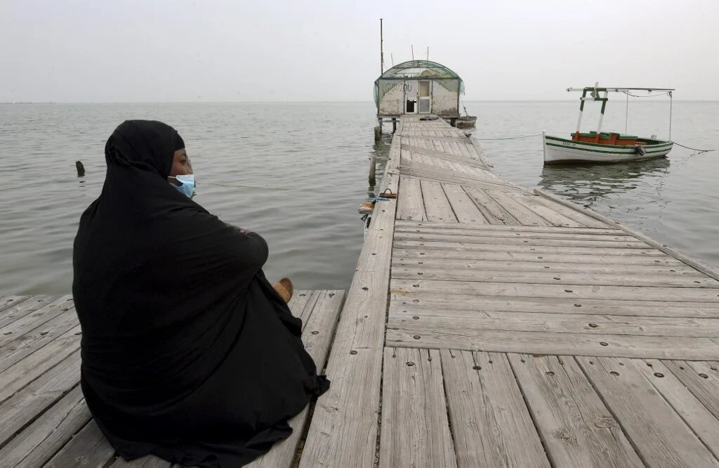 Une migrante d’Afrique subsaharienne, assise sur un ponton de Sidi Mansour, à 270 km au sud-est de Tunis, attend une opportunité pour partir en Europe (AFP/Fethi Belaïd)