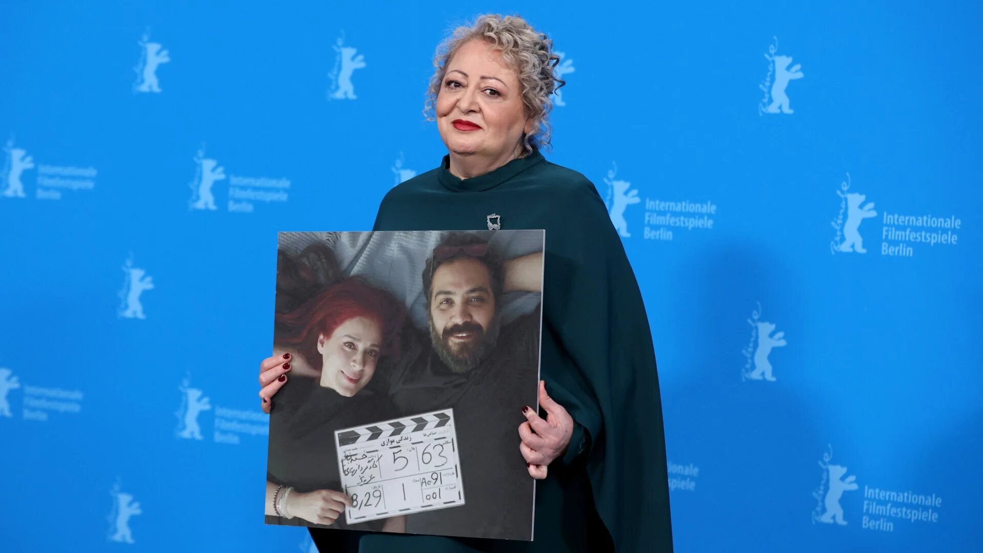 Iranian actress Lily Farhadpour holds a photograph of My Favourite Cake directors Maryam Moghaddam (L) and Behtash Sanaeeha (R) who were unable to attend the 74th Berlinale in Berlin on 16 February 2024 (AFP/Ronny Hartmann)