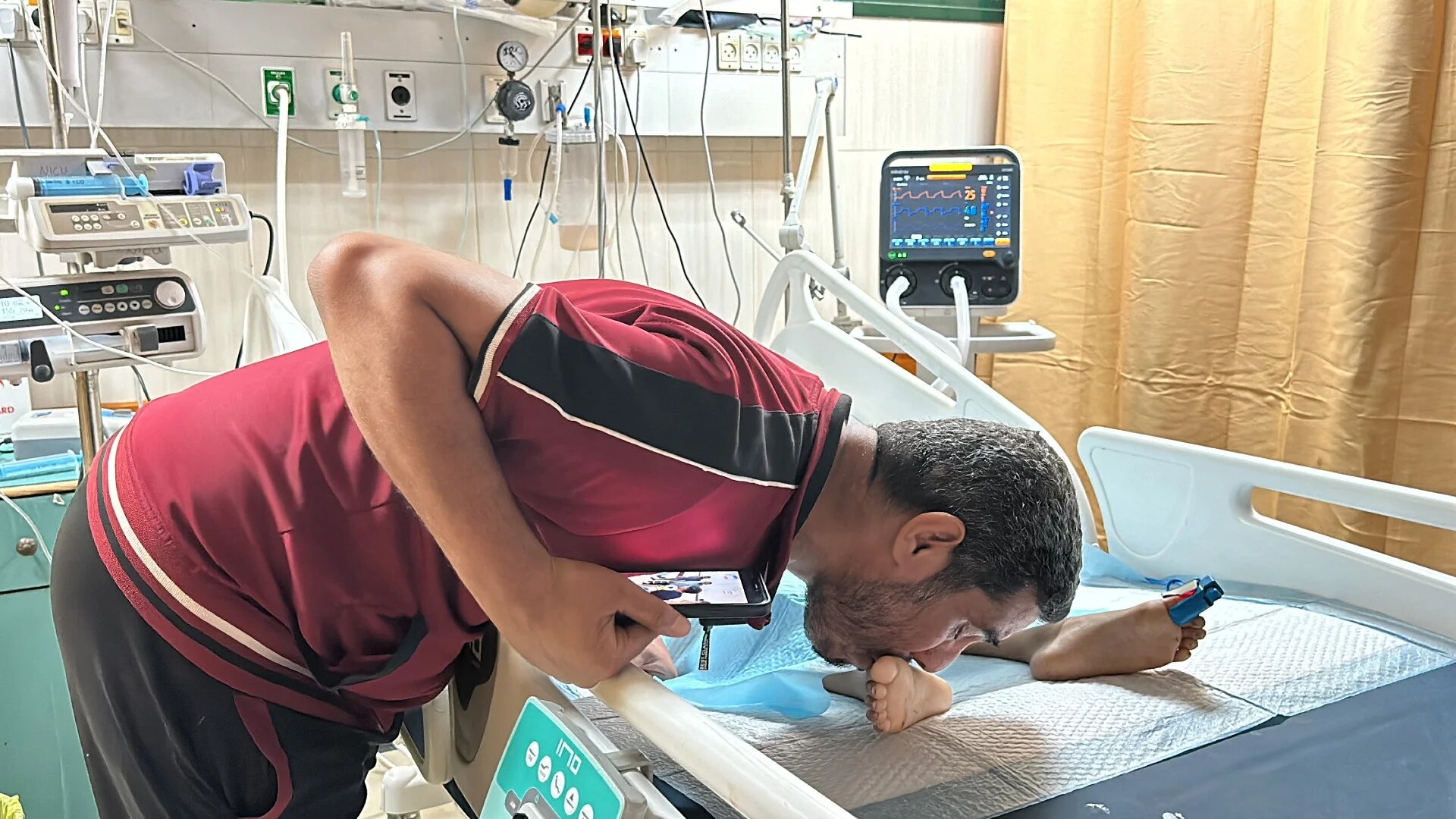 A father kisses his injured child's foot as he lies in bed at Al-Aqsa Martyrs hospital, in the aftermath of an Israeli strike on Deir al-Balah, in the central Gaza Strip, 9 June 2024 (Reuters/Doaa Rouqa)