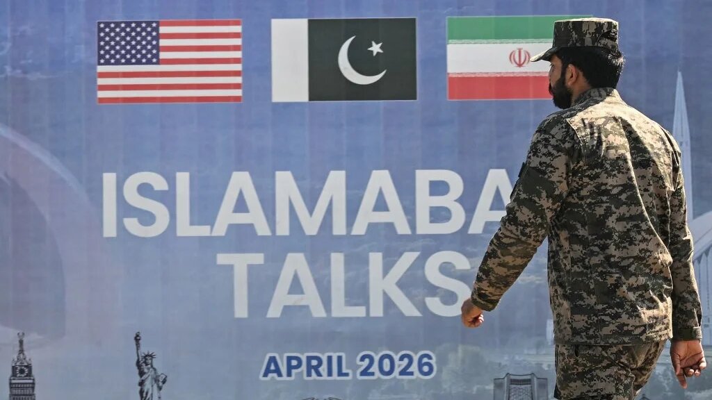 A Pakistani Ranger walks past a billboard for the US-Iran peace talks in Islamabad on 12 April 2026 (Farooq Naeem/AFP)