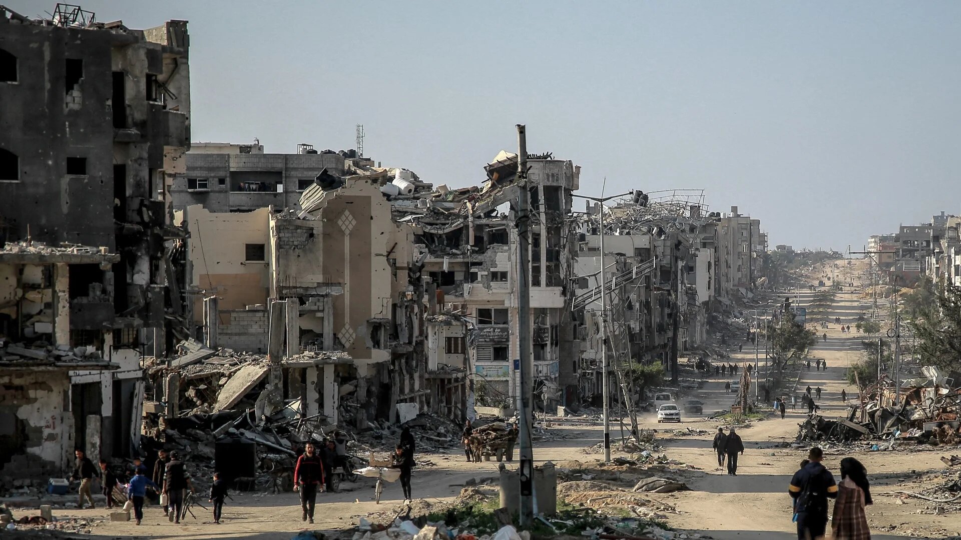 Palestinians walk past buildings destroyed by Israeli bombardment in Beit Lahia, northern Gaza, on 26 February 2024 (AFP)