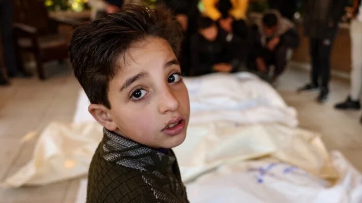 A child stands by the bodies of four members of a Palestinian family killed in an Israeli strike in the southern Gaza Strip, on 18 January 2025 (Bashar Taleb/AFP)