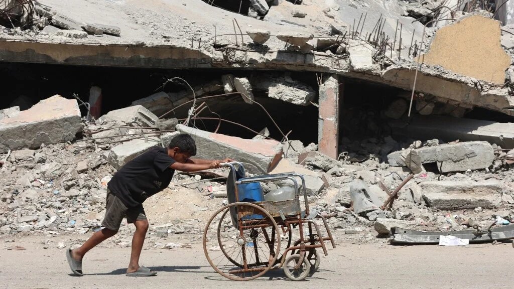 A Palestinian boy uses a wheelchair to transport plastic bottles in Gaza City on 24 August 2025 (Omar al-Qattaa/AFP)
