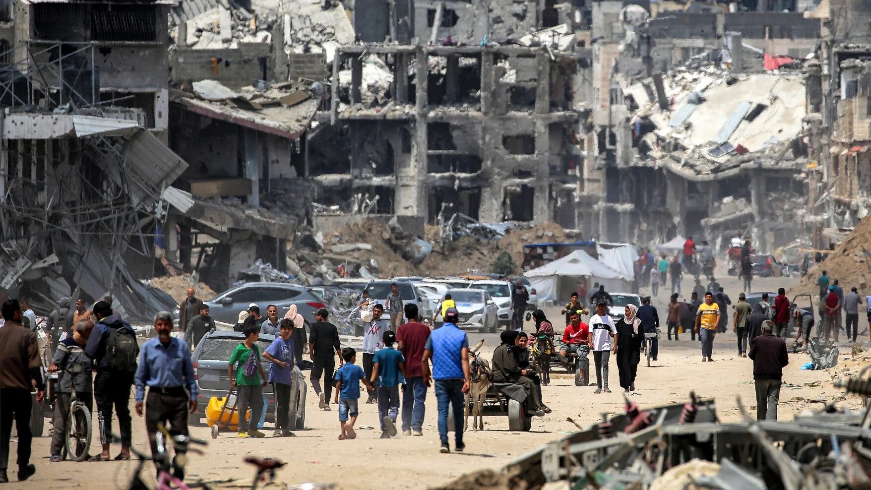 Palestinians move past destroyed buildings along a street in Khan Younis in the southern Gaza Strip on 14 May, 2024 (AFP)