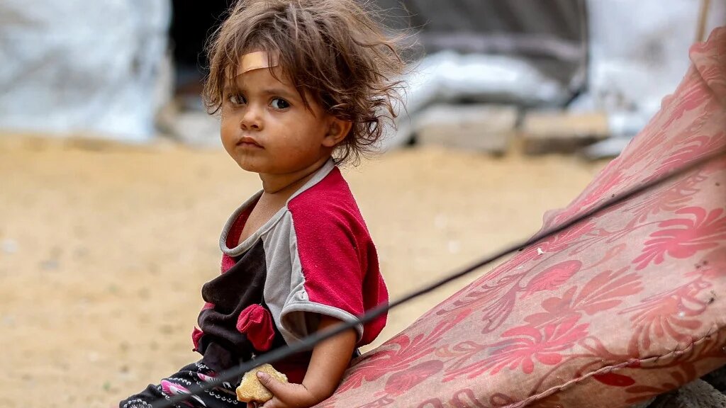A girl sits outside a tent in Khan Younis, Gaza, on 6 October 2025 (Omar al-Qattaa/AFP)