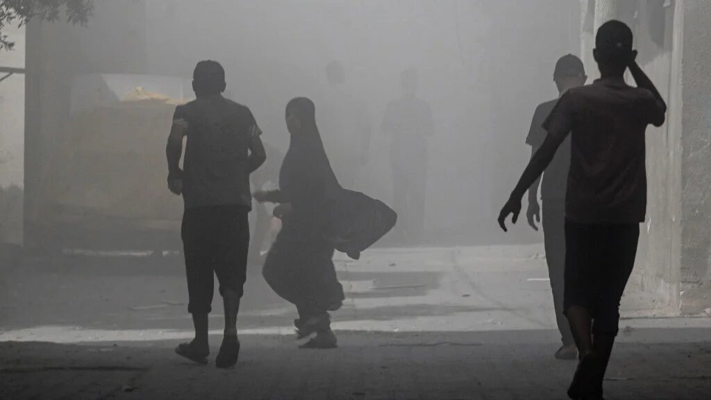 Palestinians walk through smoke and dust after an Israeli attack on Gaza’s Nuseirat camp on 8 June 2024 (Bashar Taleb/AFP)