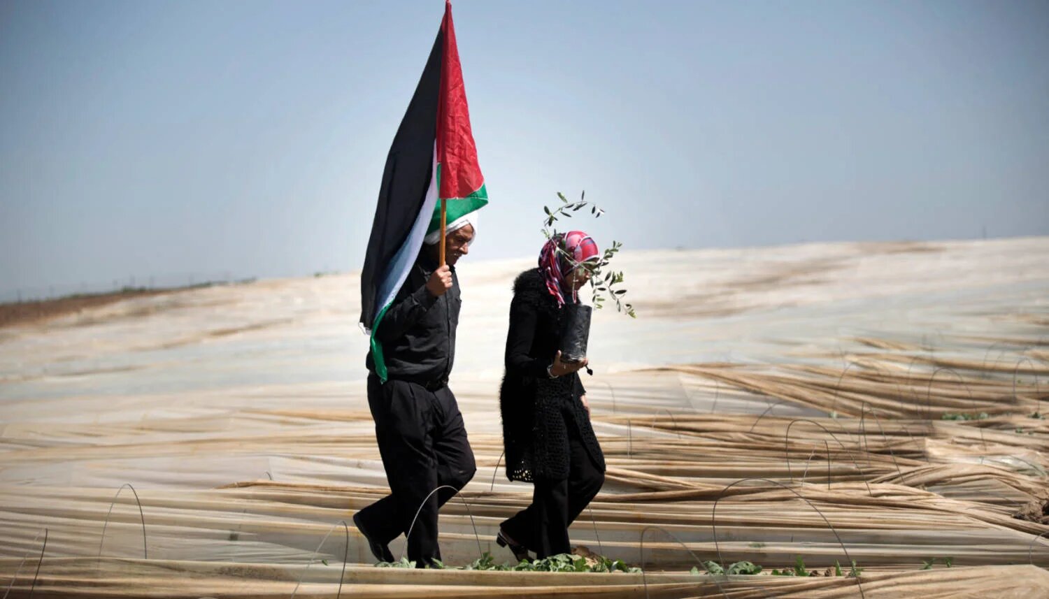 A Palestinian man holds a flag and a Palestinian woman carries an olive tree to mark Land Day near Jabalia, Gaza, in March 2014 (AFP)