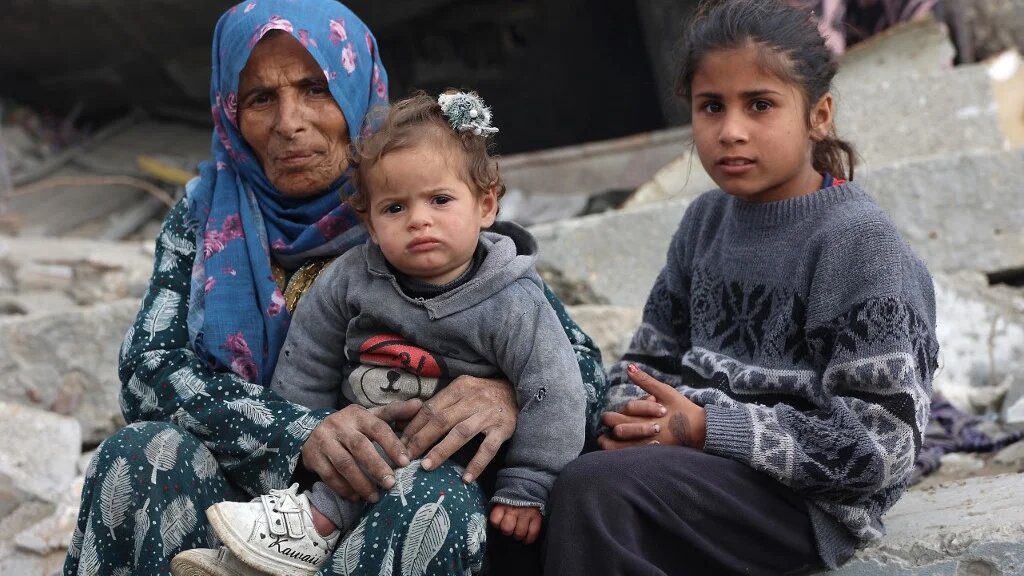 A Palestinian woman and children sit amid the rubble of destroyed buildings in Jabalia, northern Gaza, on 5 February 2025 (Omar al-Qattaa/AFP)