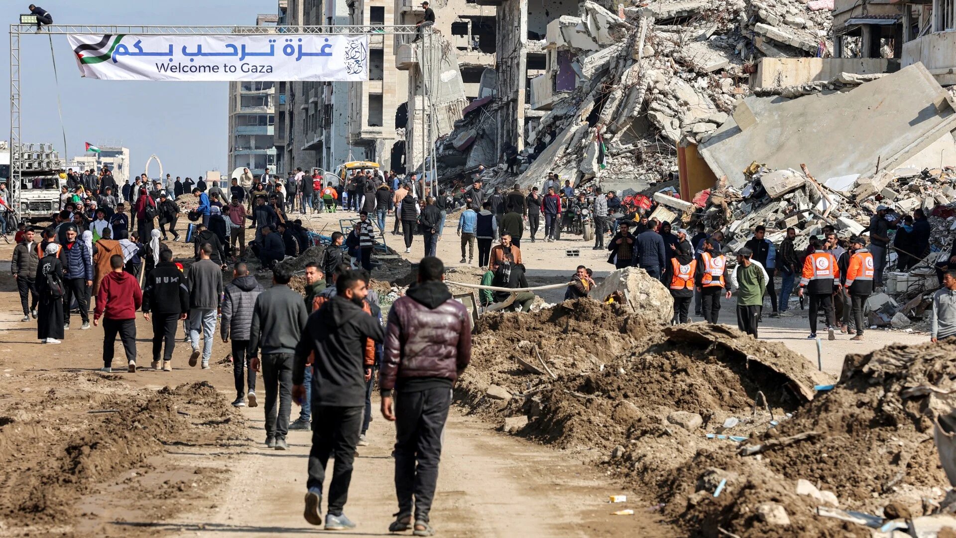 Palestinians walk past a banner welcoming people along Rasheed Street into Gaza City on 26 January 2025 (Omar Al-Qattaa/AFP)